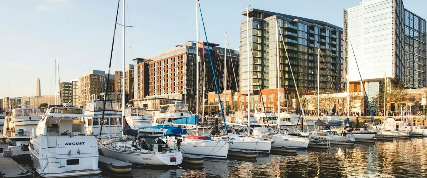 A row of boats docked along the Wharf, with modern buildings in the background and golden light. 
