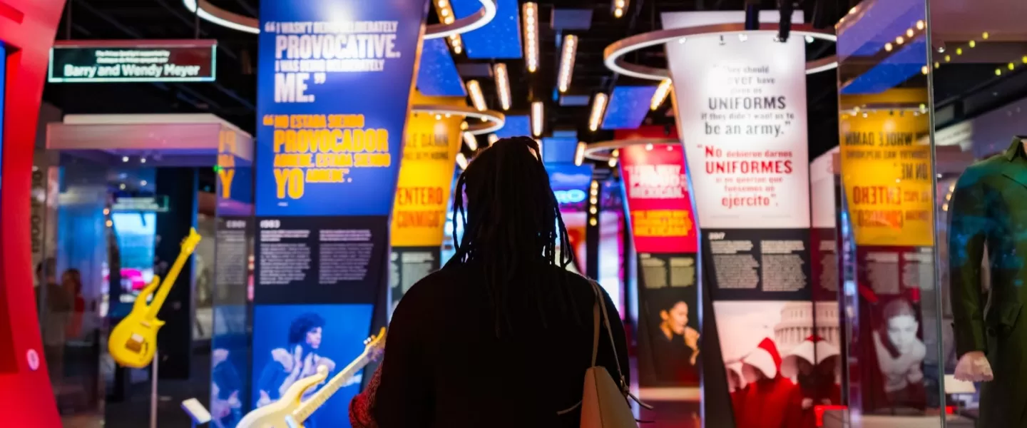 A visitor walks through a colorful and immersive exhibit at the National Museum of American History, featuring guitars, quotes and historic pop culture displays.