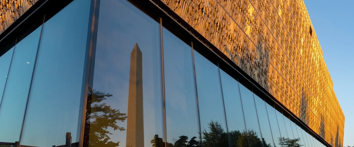 Modern glass building with obelisk reflected, golden facade in evening light