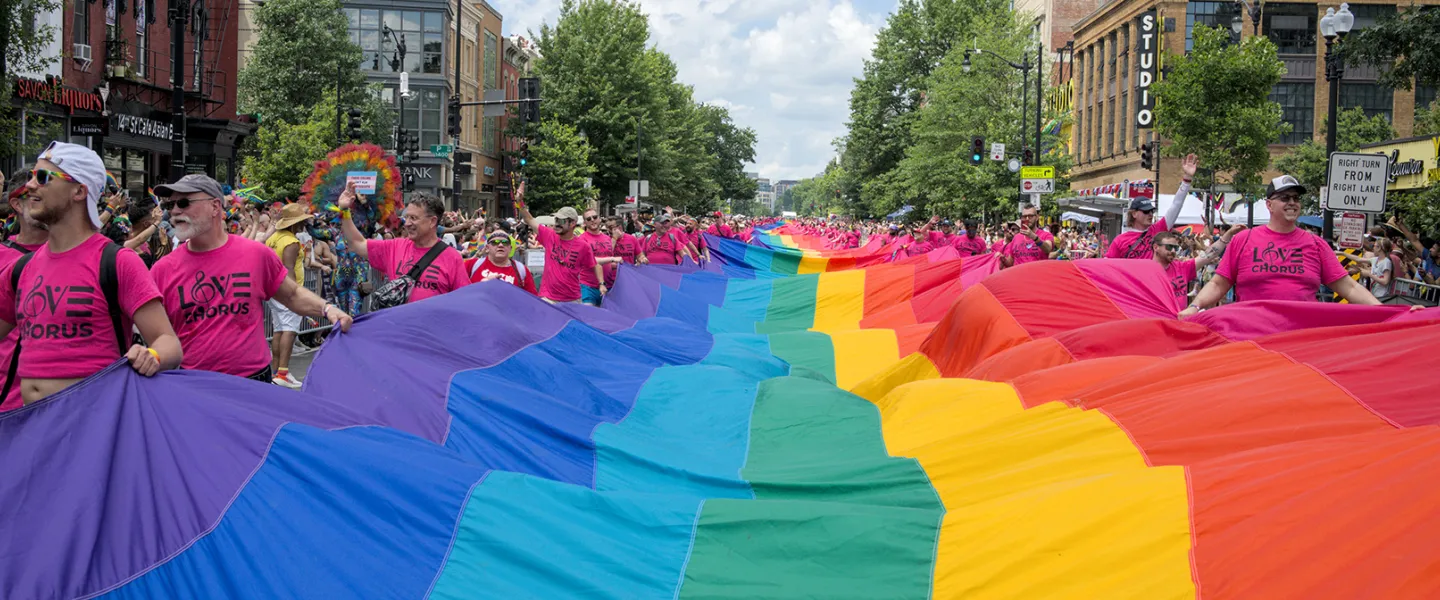 People holding a long rainbow fabric banner across a city street during a march