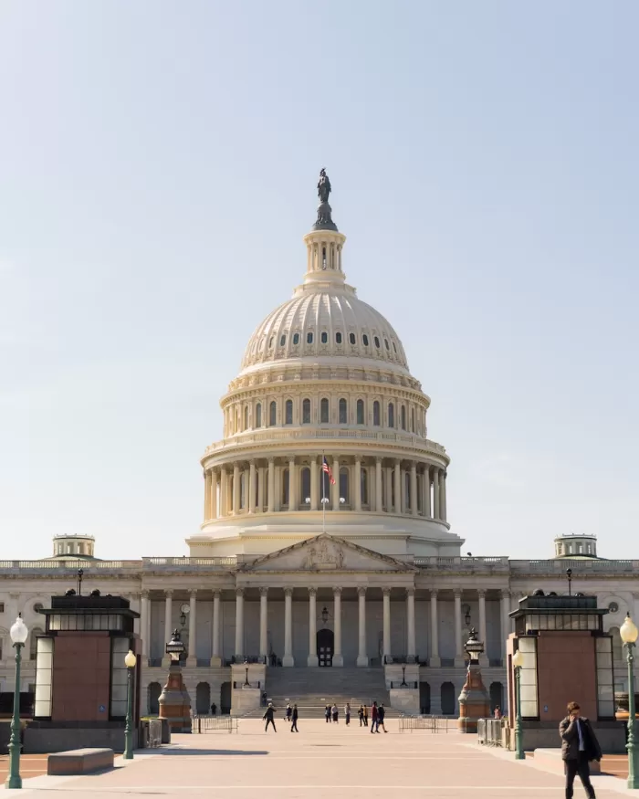 The U.S. Capitol building on a bright, summer day with people walking on the sidewalk below. 