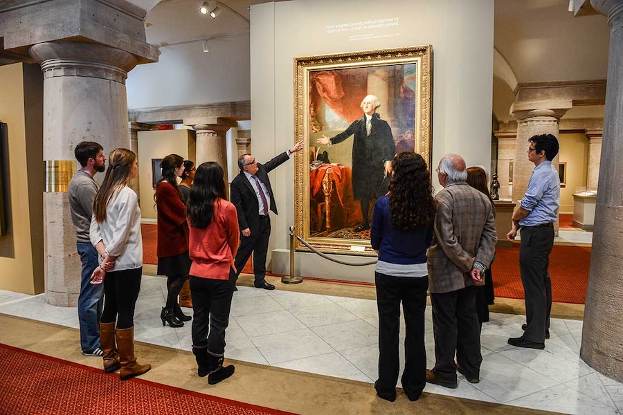 A group listens to a guide explaining a portrait of George Washington at a museum in Washington, DC.