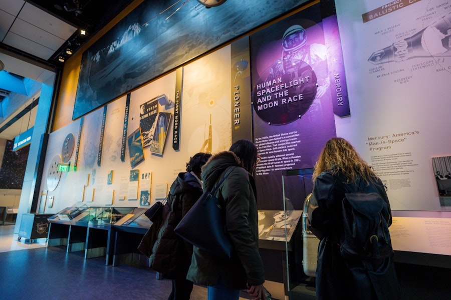 Three women explore an exhibition on human spaceflight and the moon race, featuring colorful wall displays at the National Air and Space Museum.