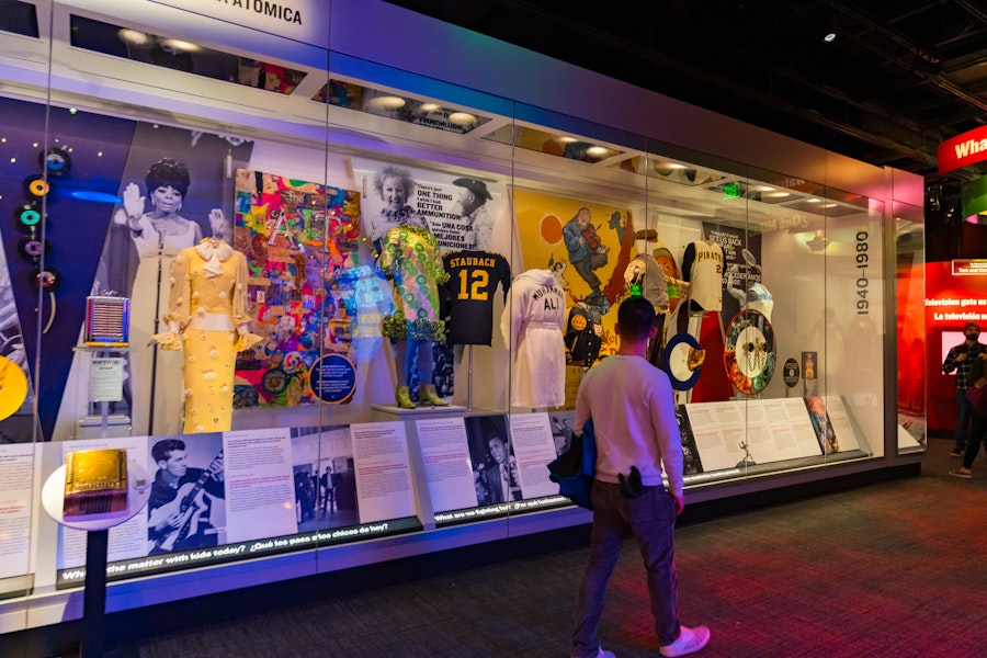 A visitor looks at a display of retro outfits, sports memorabilia and cultural icons behind glass at the National Museum of American History.