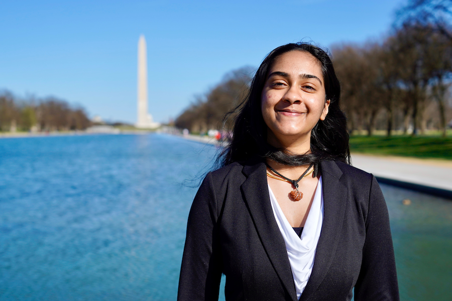 A young woman stands smiling in front of the Reflecting Pool in Washington, D.C., with the Washington Monument in the background.