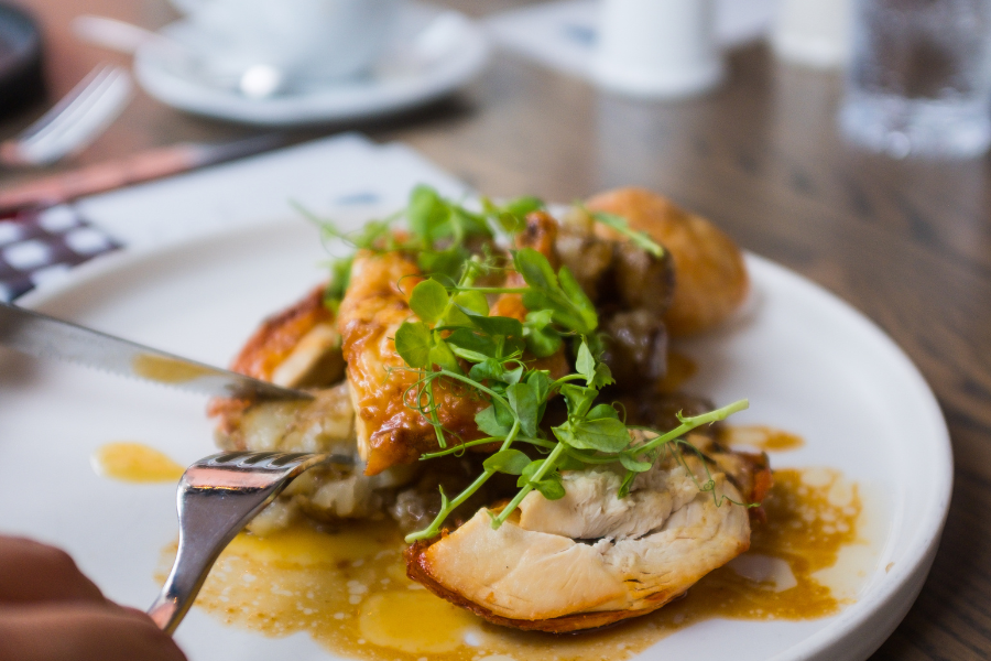 A close-up of a juicy roast chicken dish topped with fresh greens at Nina May in Washington, DC.