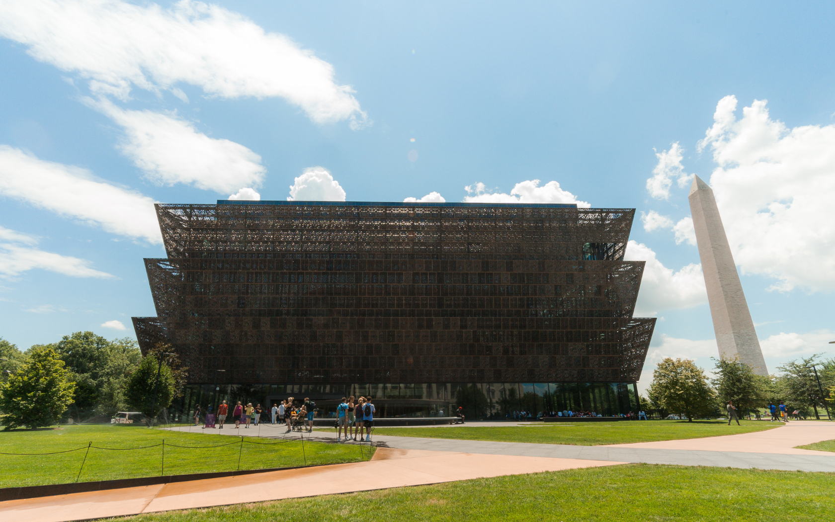 The Smithsonian National Museum of African American History and Culture stands out under a sunny sky with the Washington Monument visible in the background.