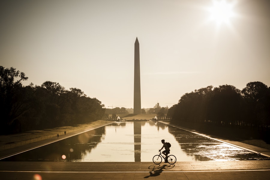 A cyclist rides past the Reflecting Pool with the Washington Monument rising in the background at sunrise.