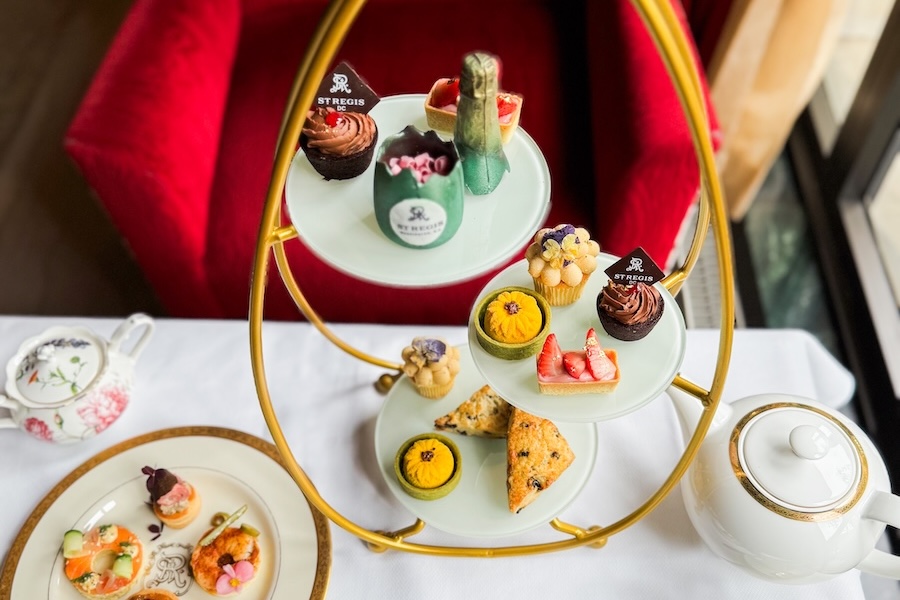 A tiered stand of pastries and tea sits on a white tablecloth in a luxurious setting.