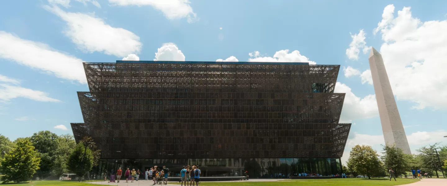The Smithsonian National Museum of African American History and Culture stands out under a sunny sky with the Washington Monument visible in the background.