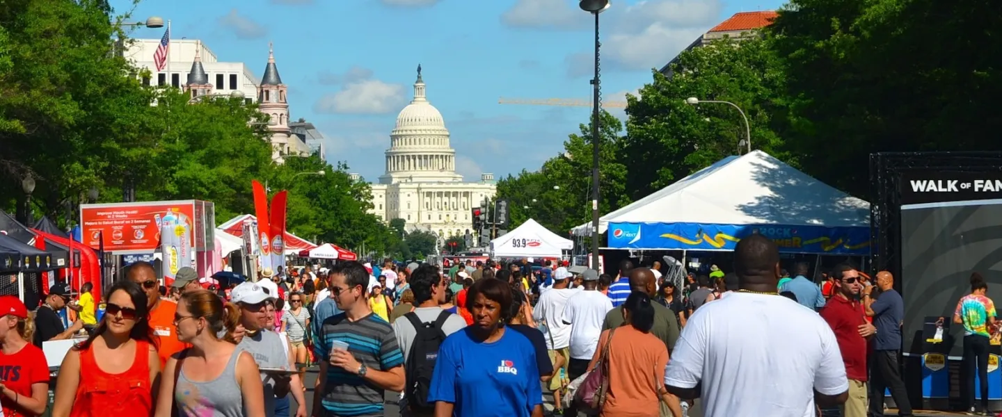 Crowds on Pennsylvania Avenue with BBQ grills, smoke and live music stage. 