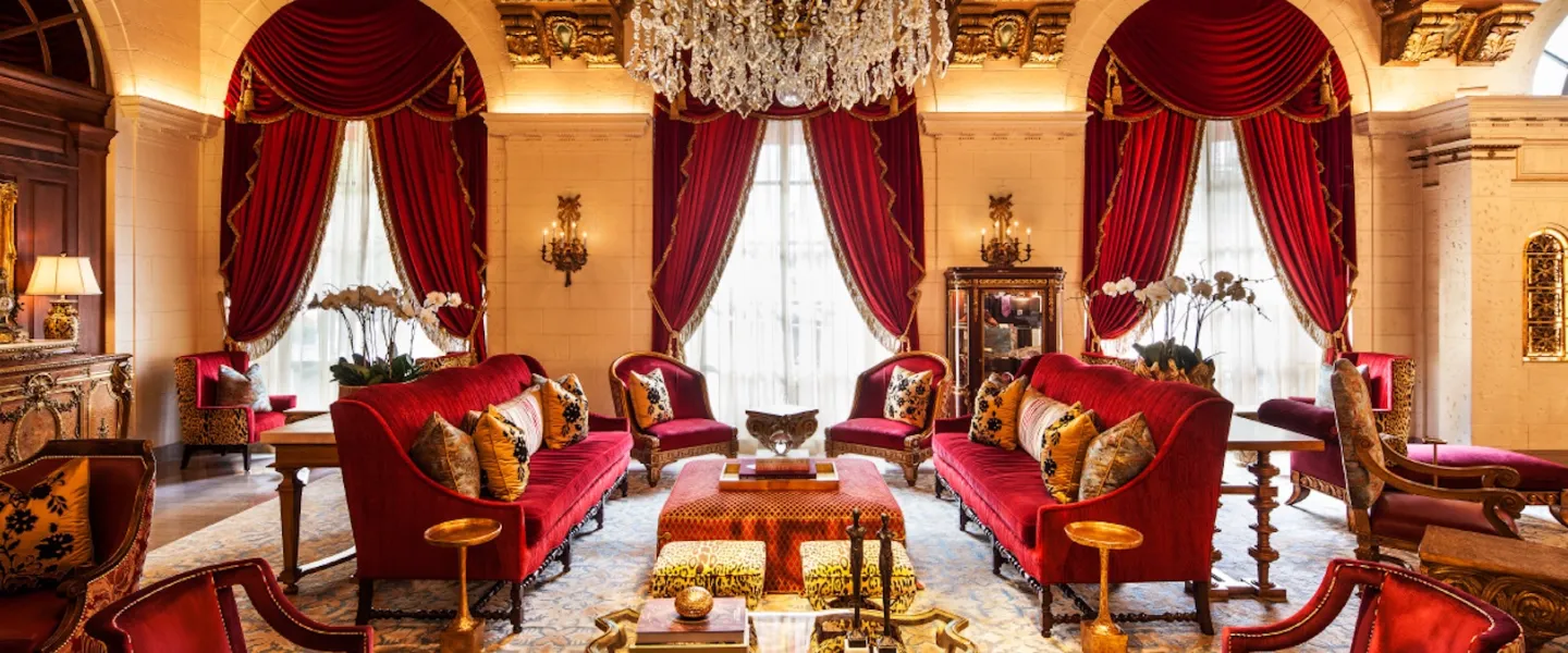 An elegant hotel lobby, decorated with rich red velvet, gold accents and a stunning chandelier.