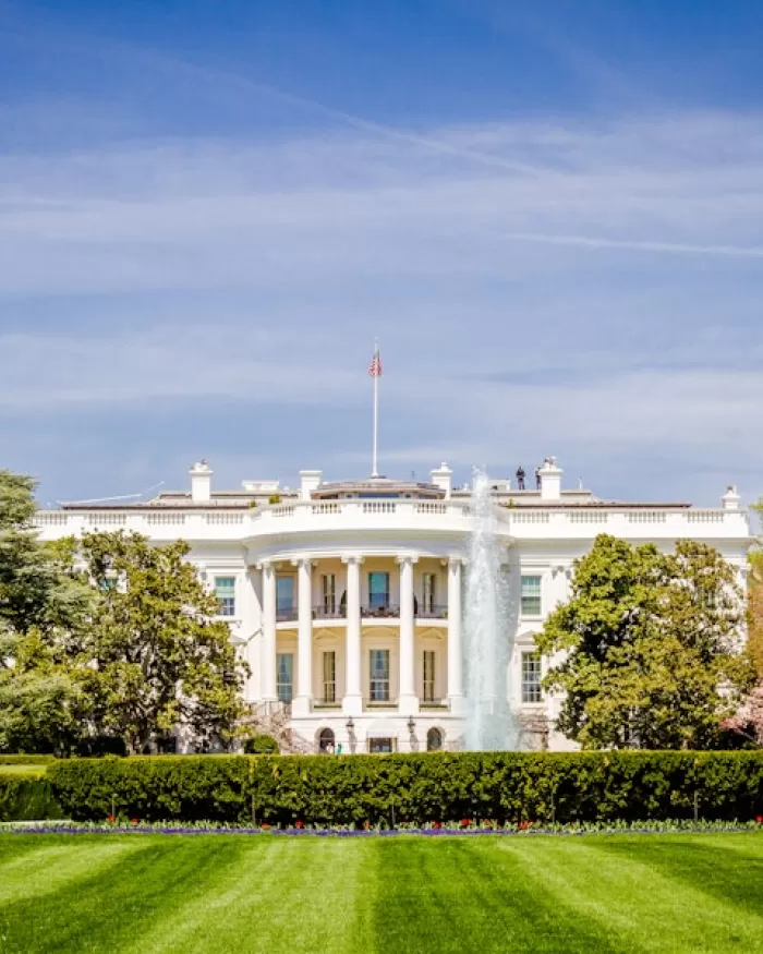 The White House with a green lawn, running fountains and trimmed bushes in front. 